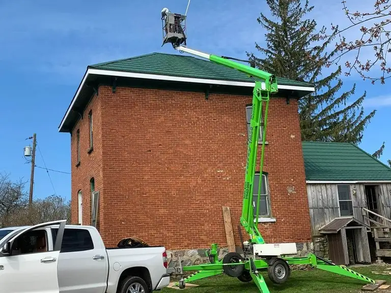 A green crane in front of a red brick building on a Cruickshank Flat Roofing job